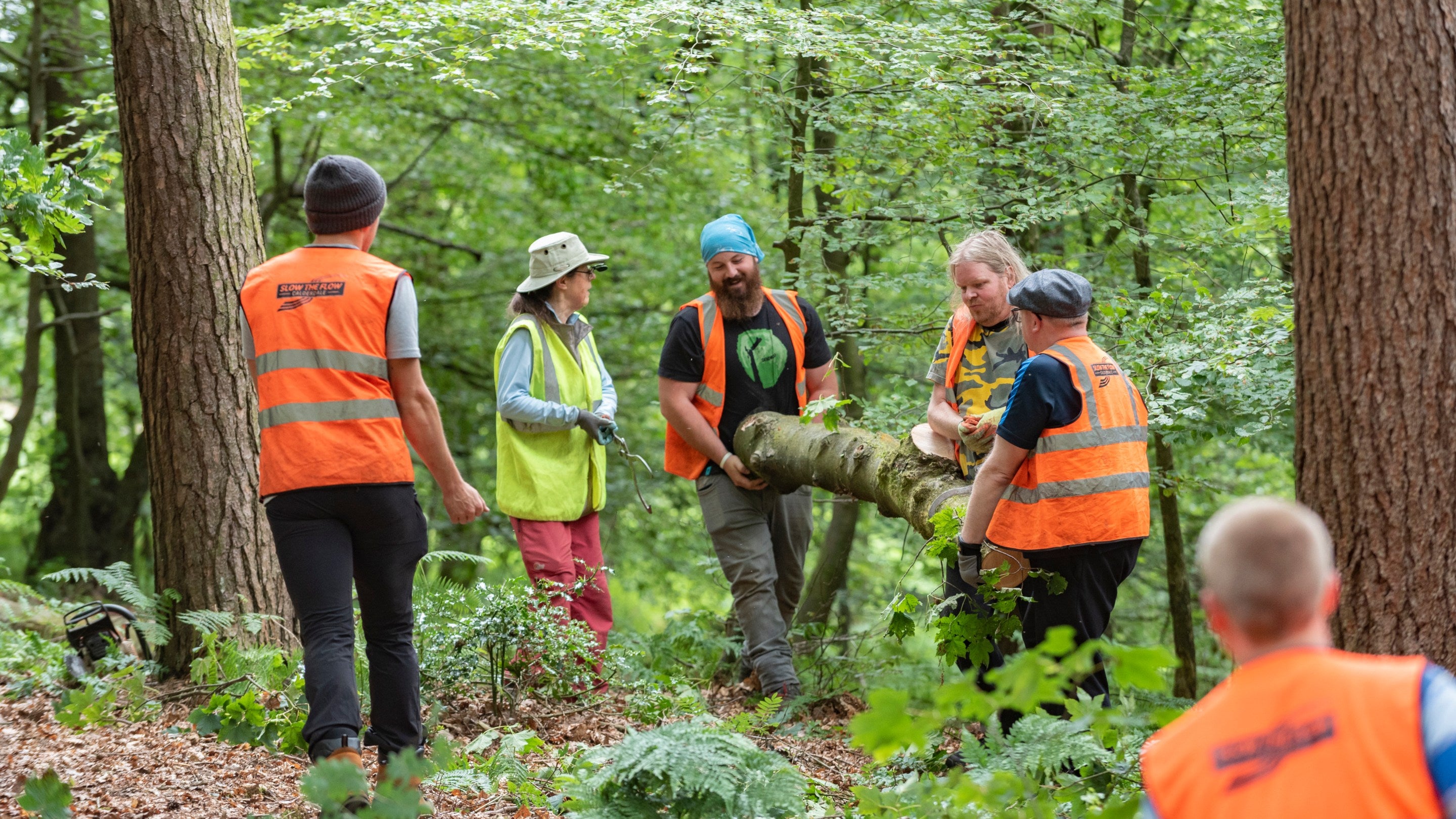 Six volunteers in high-vis jackets lifting a log at Hardcastle Crags, Yorkshire
