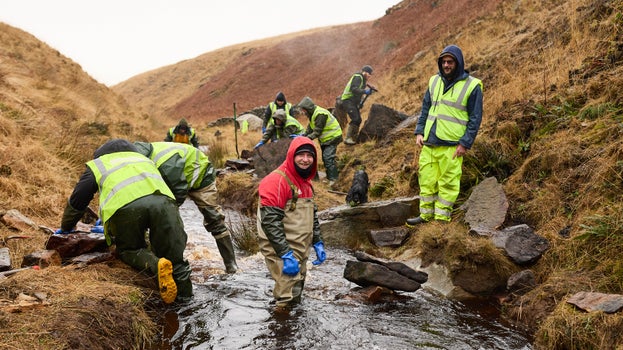 A group of men stand in a stream while making a dry stone wall to stop floodwater on Marsden Moor