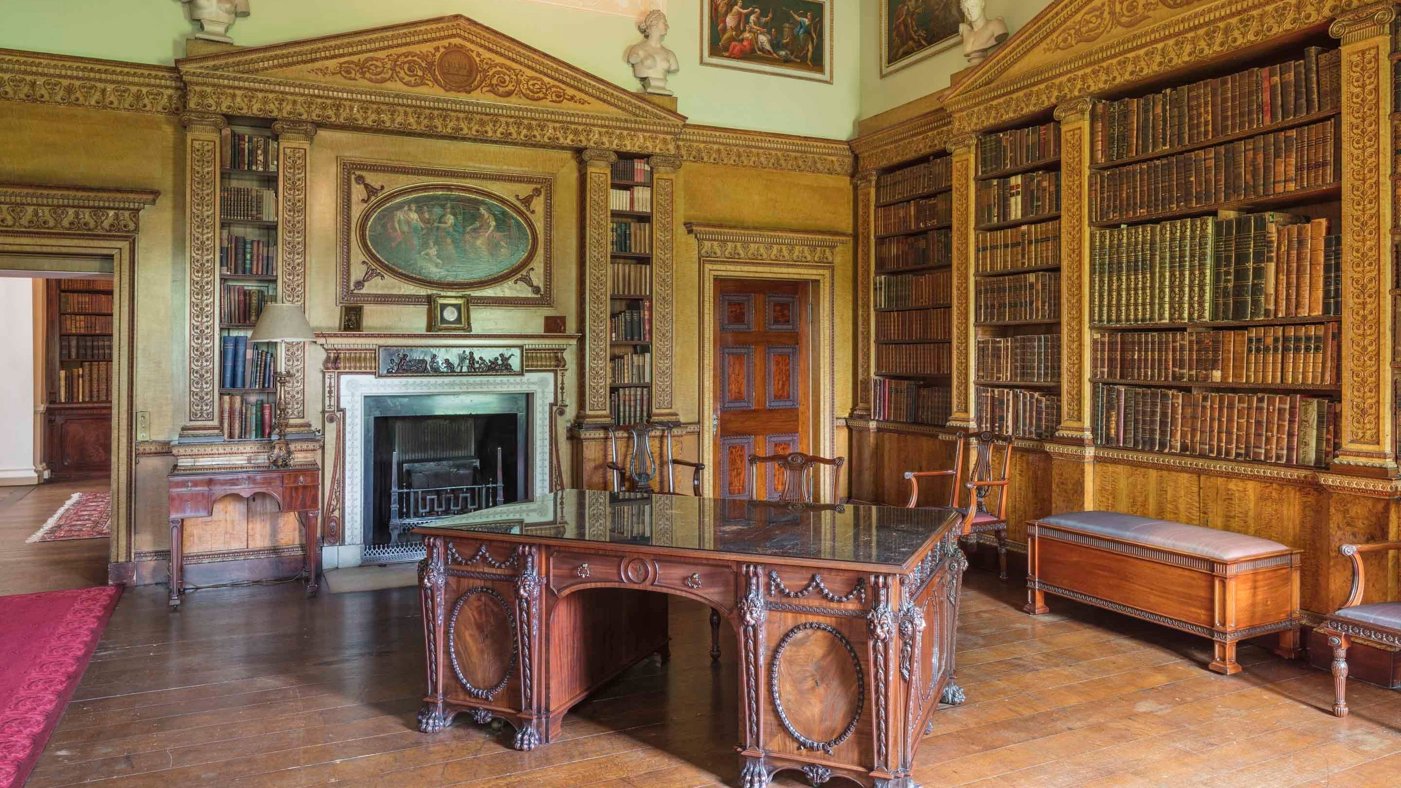 The interior of the library at Nostell Priory showing a large desk and ornate bookcases on the walls