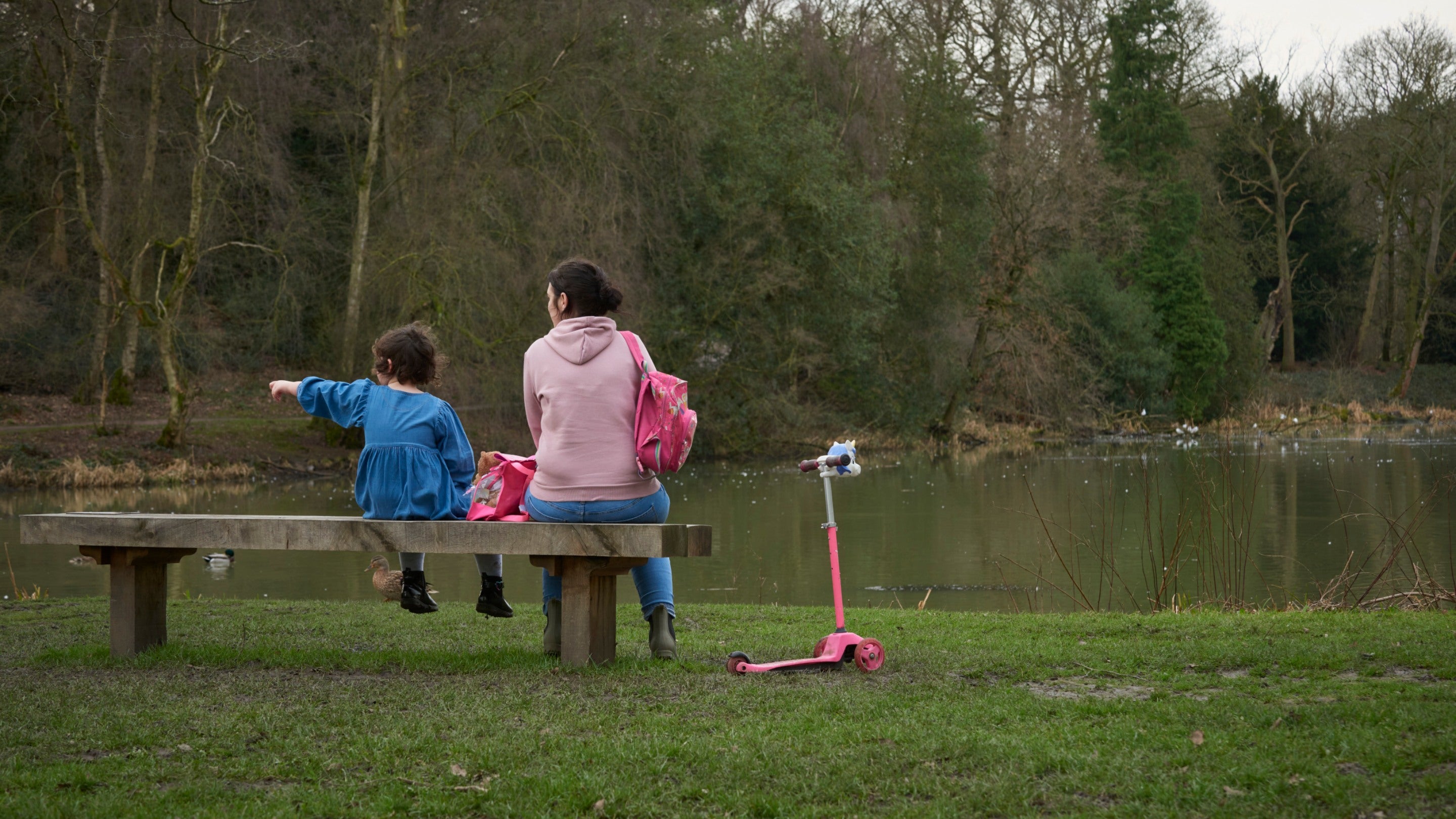 Parent and child sit on a bench looking out over the lake in the parkland at Nostell