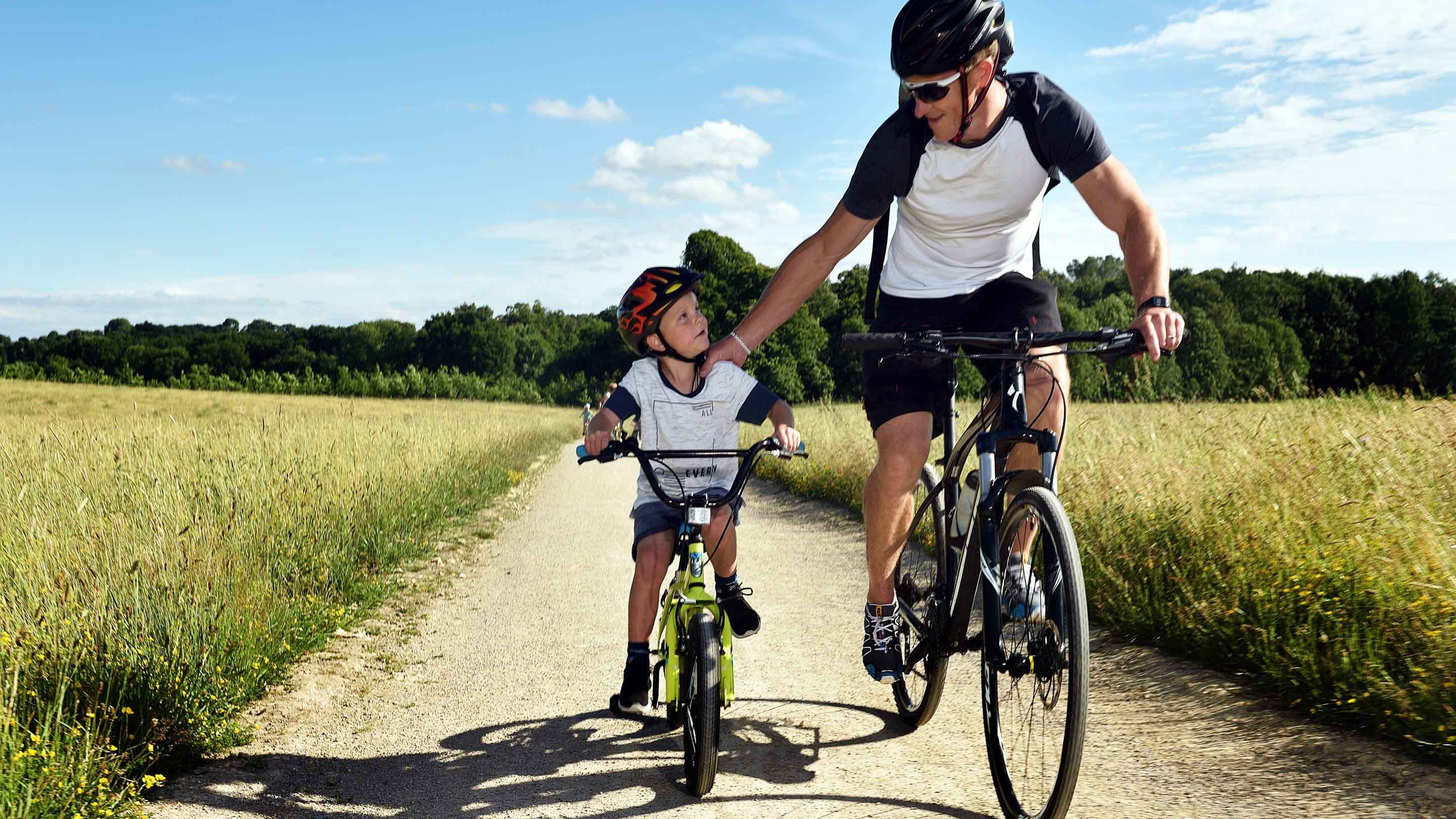 An adult and a young boy riding their bikes on a path at Nostell Priory