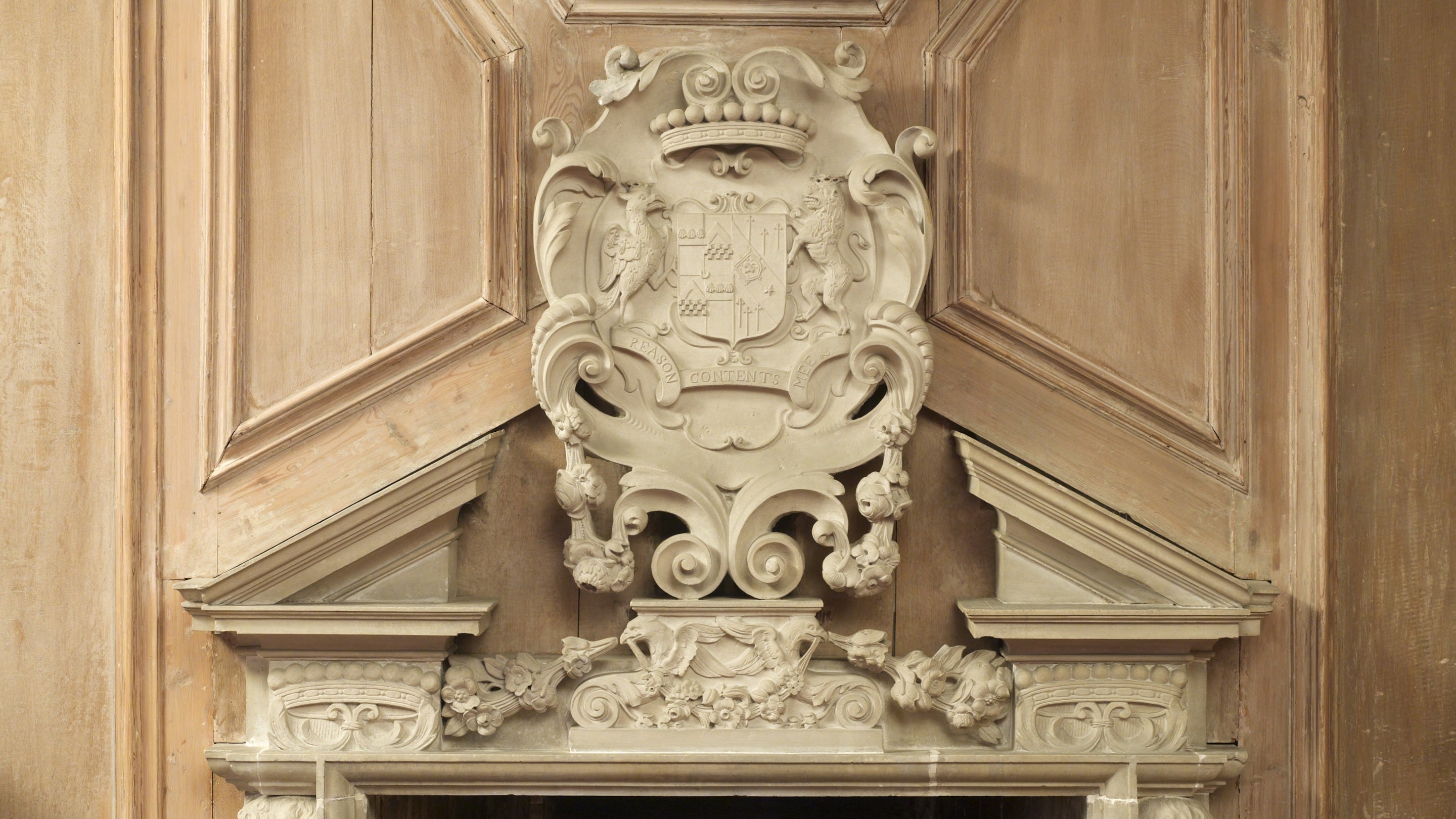 Details of a stone coat of arms on oak panelling over fireplace