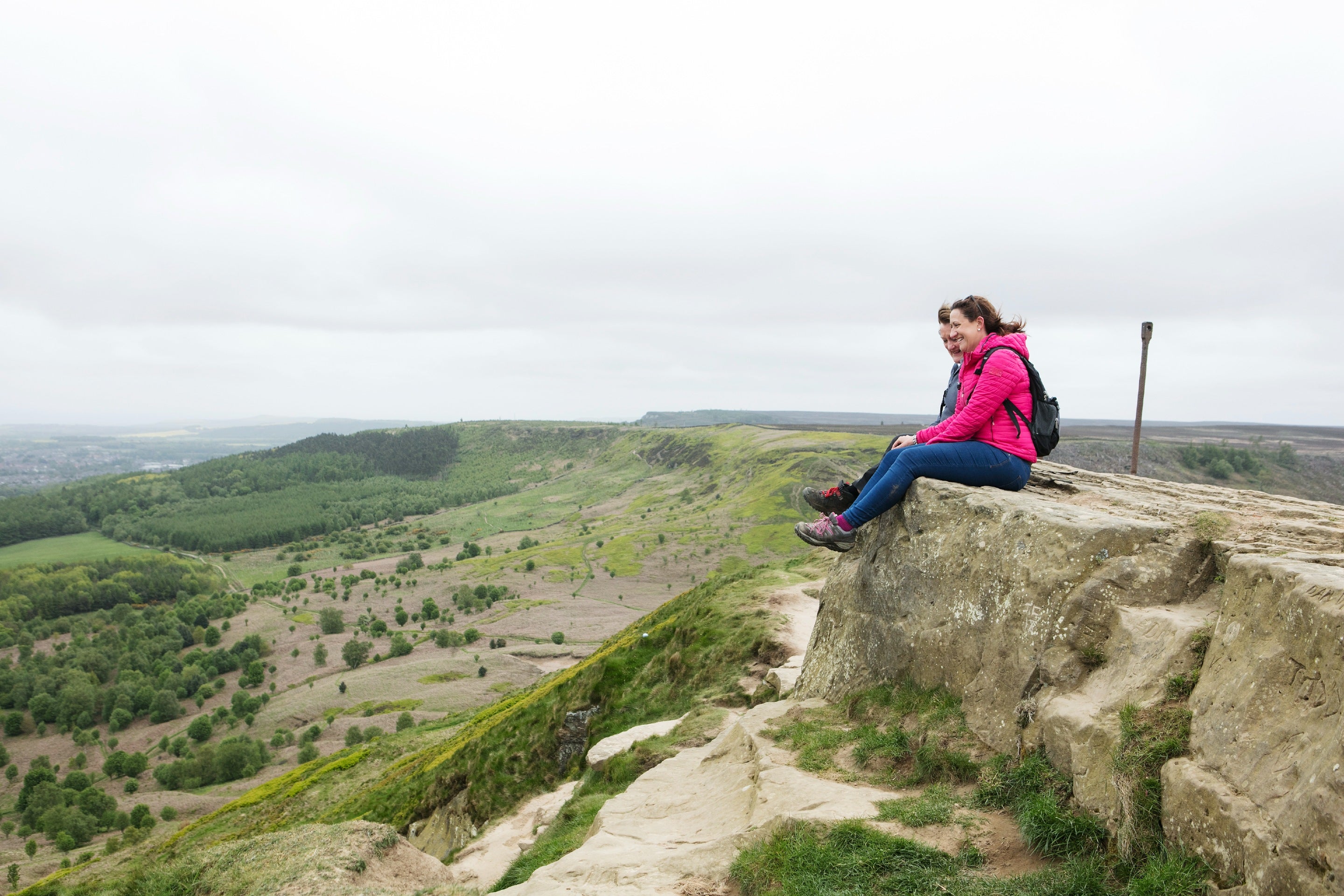 Two women sitting on top of a rocky outcrop with expanding scenery below them