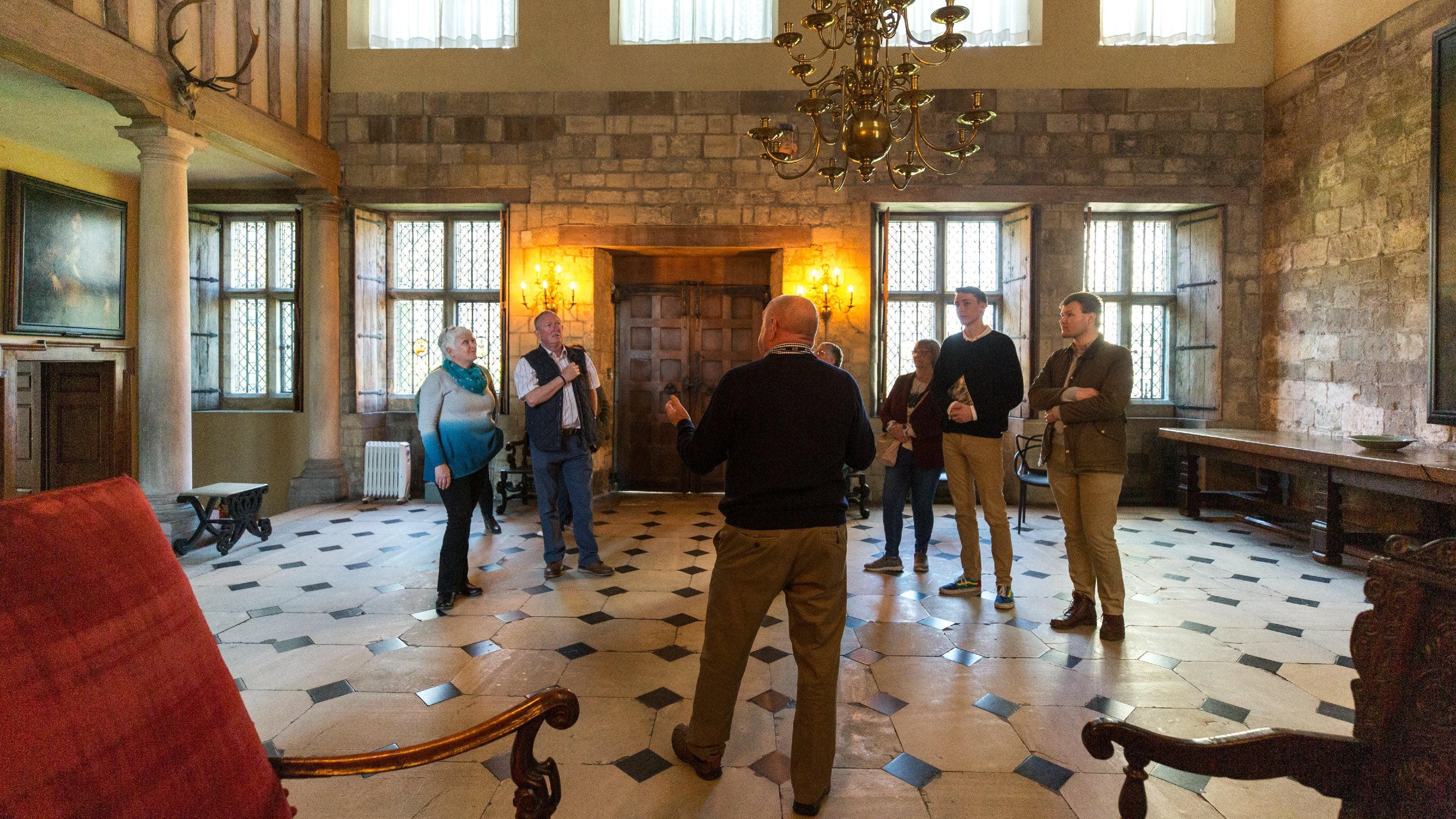 Group of people standing around listening to a guide in a large stone hall