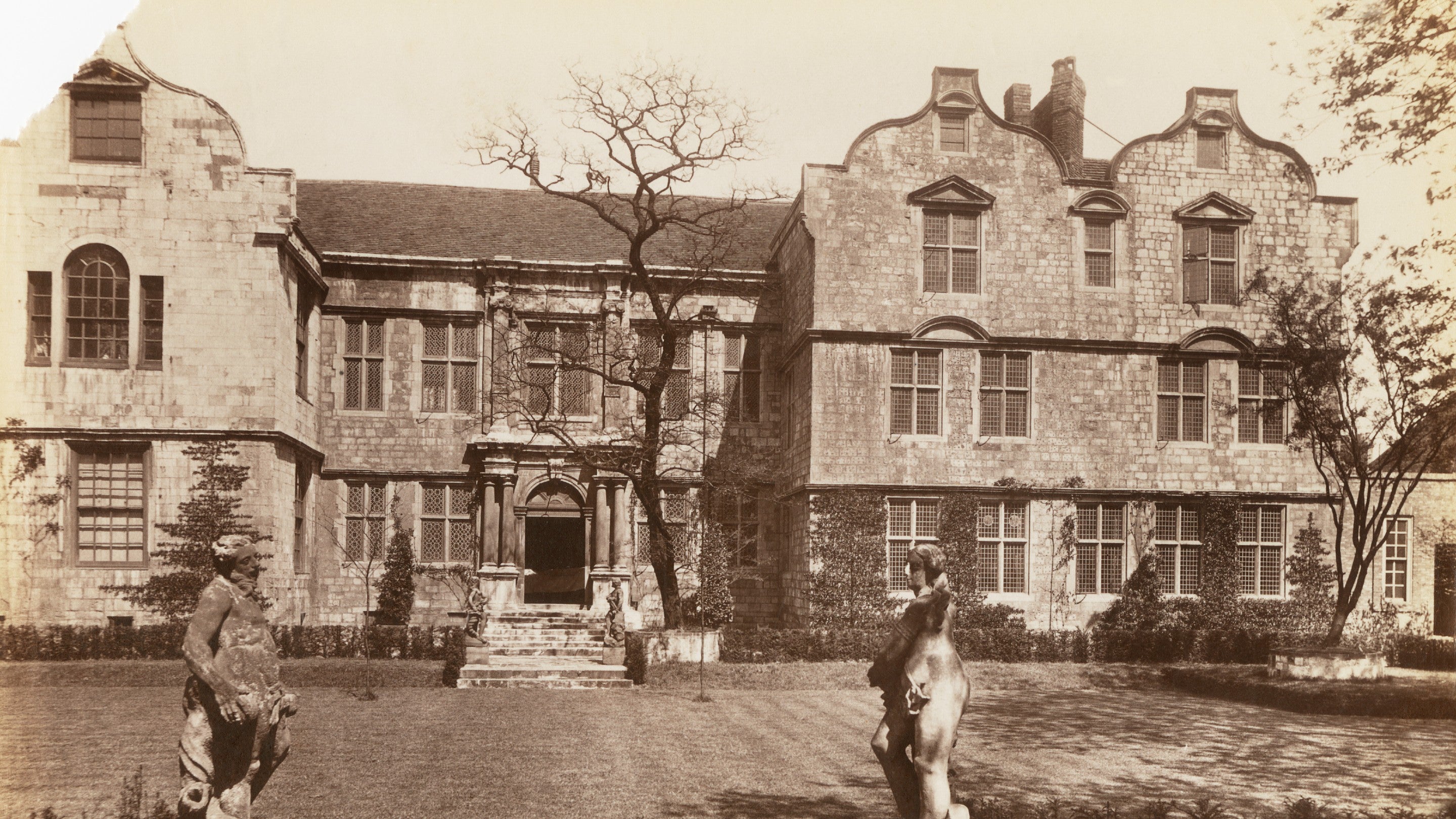 Sepia image of a stone house and lawn with statues in the garden
