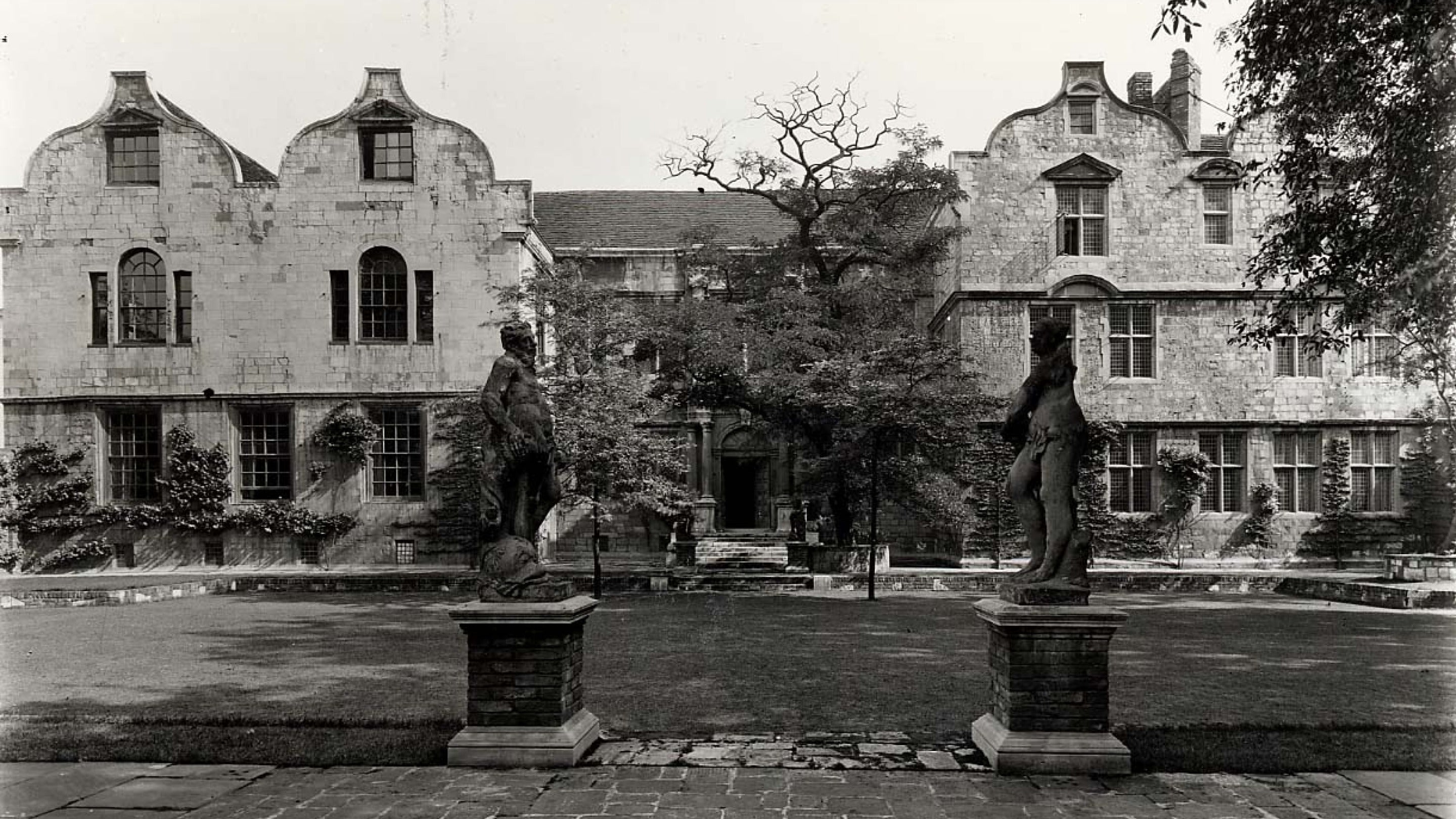 Historic black and white photo of a large house with garden and statues