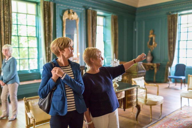 Two visitors point at a mirror out of frame in a gold and blue drawing room