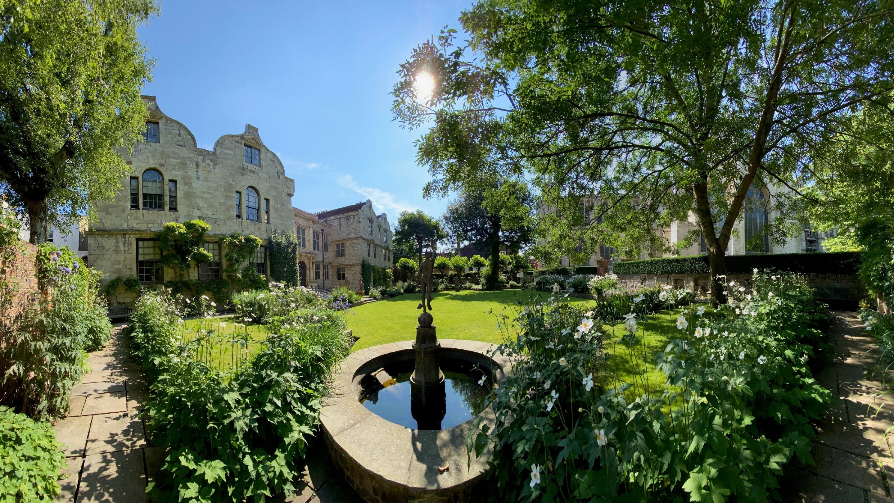 View on a sunny day with a fountain stature in the foreground and lawn, trees and blue sky beyond