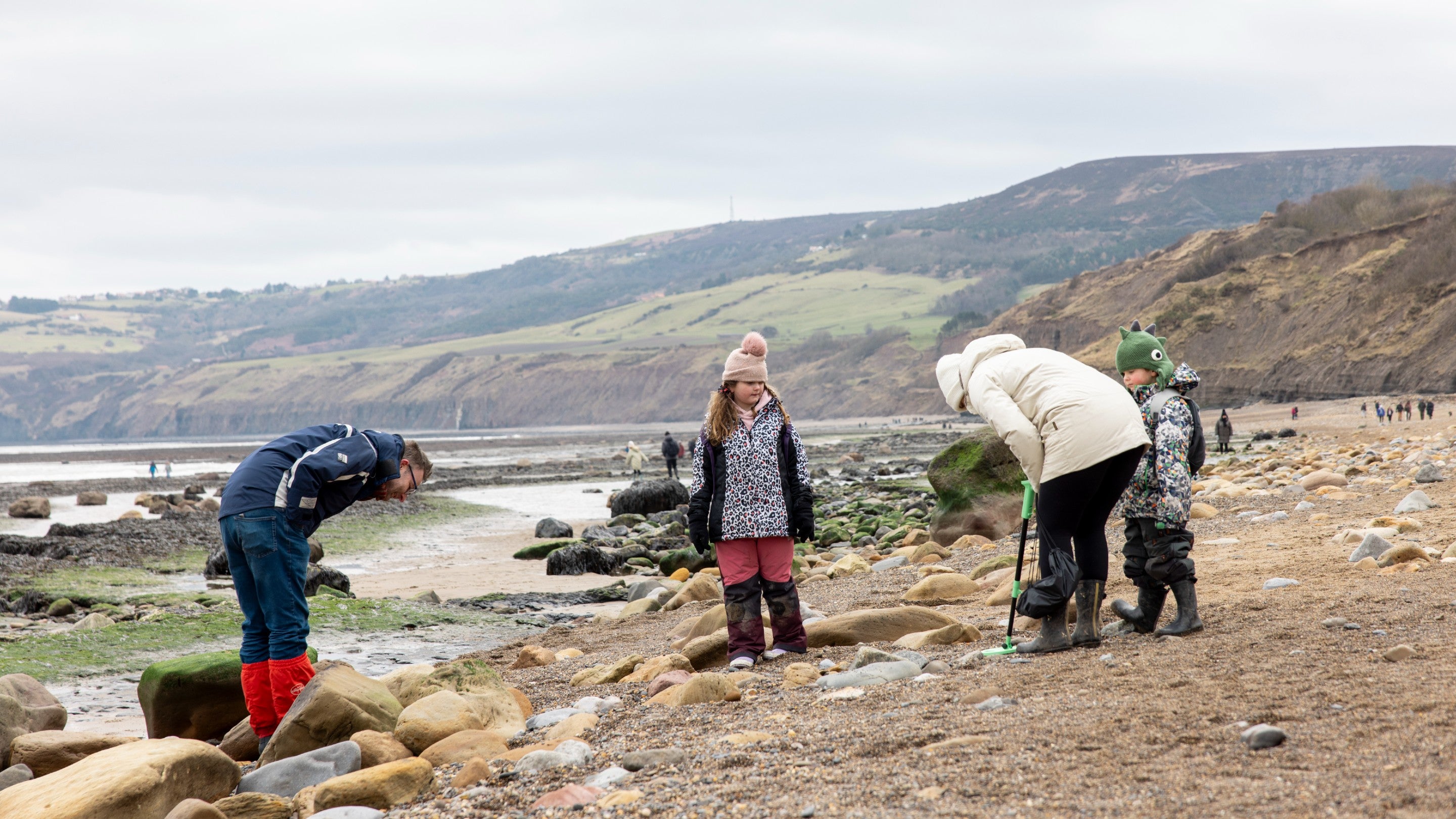 Winter scene of family beachcombing at low tide on beach at Robin Hood's Bay
